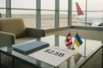 Папки с документами и заметка «$2.5B» рядом с маленькими флажками Канады и Украины в зале аэропорта