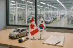 Флаги Канады и Южной Кореи рядом с макетом электромобиля и зарядным штекером на столе в светлом цехе