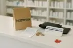 Касса аптеки в Канаде: чек с высокой суммой за рецепт, монеты и приоткрытый кошелёк на стойке