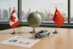 На столе в офисе глобус и миниатюрный электромобиль между флагами Канады и Китая, дневной свет