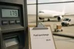 Экран оплаты на заправке и чек с строкой «топливная надбавка» на фоне аэропорта и посылок в Канаде