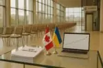 Стол с документами о пакете помощи, маленькие флажки Канады и Украины в светлом зале саммита