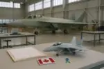 Светлый авиационный ангар в Канаде: на переднем плане макет истребителя и папка документов, нейтрально.