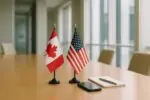 Два настольных флага Канады и США рядом со смартфоном экраном вниз в светлой переговорной, дневной свет