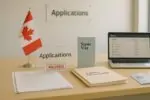 Светлый офис госслужб Канады: папки «Family Sponsorship» и табличка «Paused», рядом брошюра Super Visa.