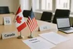 Стол переговоров с флажками Канады и США, документами о тарифах и спокойным дневным светом
