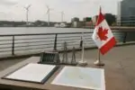 Папка с соглашением и макет ГЭС, ЛЭП и ветряка на фоне тихой канадской гавани при дневном свете