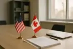 Флаги США и Канады у деловых документов и графиков на столе в светлом офисе, символ спора о торговле