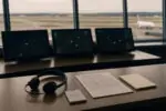 Пустая диспетчерская авиадиспетчеров с гарнитурой и экранами радара на фоне взлётной полосы днём
