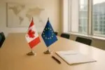 Флаги Канады и ЕС рядом на столе переговоров в светлом зале, символизируя расширение сотрудничества