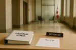 Папка «Labour Code», лист «Bill C-39» и табличка «Section 107» в светлом холле суда, без людей.