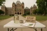 Стол с банкой речной воды и табличкой «Stop Mercury» на фоне Куинс‑Парка в Торонто, дневной свет