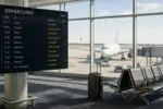 Тихий зал аэропорта с табло вылетов, где видны отменённые рейсы в США, и самолёт за окном.