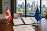Флаги Канады и ЕС по разные стороны от папки с черновиком соглашения на столе, мягкий дневной свет.