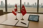 Флаги Канады и Турции на столе рядом с папкой соглашения в светлой переговорной, нейтральный фон